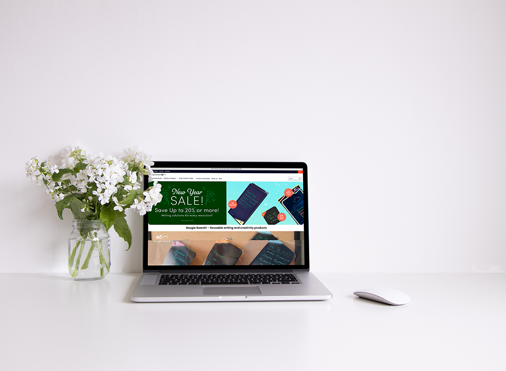A modern workspace featuring a laptop displaying a promotional website for writing solutions, alongside a white mouse and a vase of fresh flowers, creating an inviting and organized aesthetic.