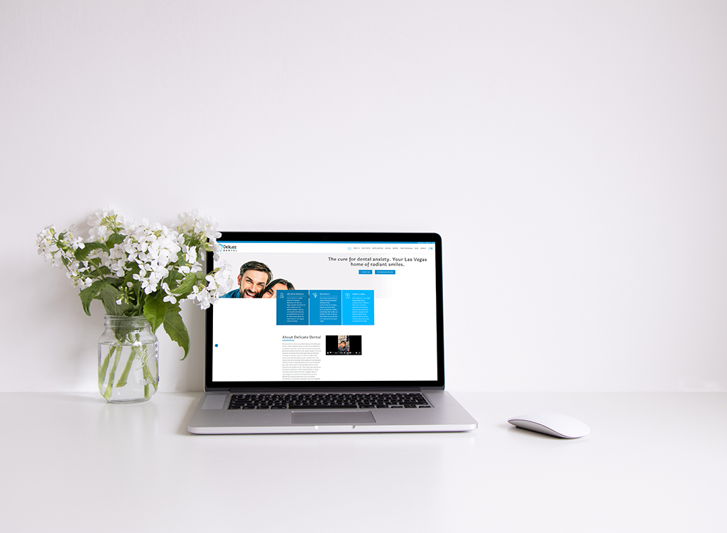 A laptop displaying a dental website with a bright, modern design sits on a clean white desk next to a vase of white flowers, symbolizing a fresh and inviting atmosphere for dental care services.