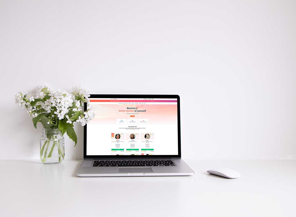 A modern laptop displaying a motivational website with the phrase "Become a better version of yourself," next to a jar of white flowers on a clean, minimalist desk.