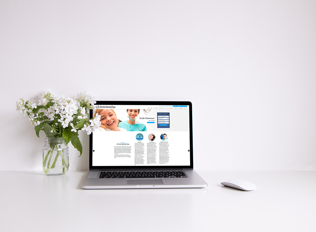 Laptop displaying the Smile Dental Spa website, featuring a dental makeover section, alongside a vase of white flowers on a minimalist desk.