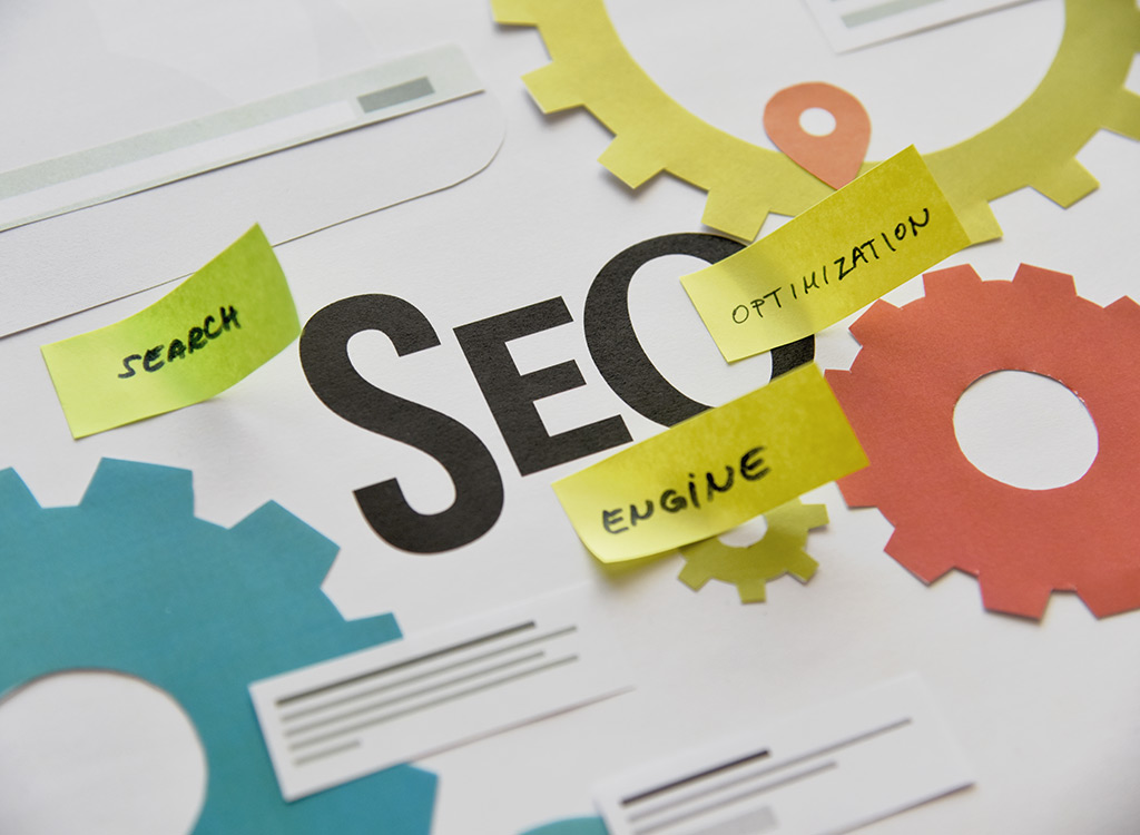 Illustration of SEO concepts featuring the word "SEO" prominently displayed with colorful gears and sticky notes labeled "Search," "Engine," and "Optimization," symbolizing key components of search engine optimization strategies.